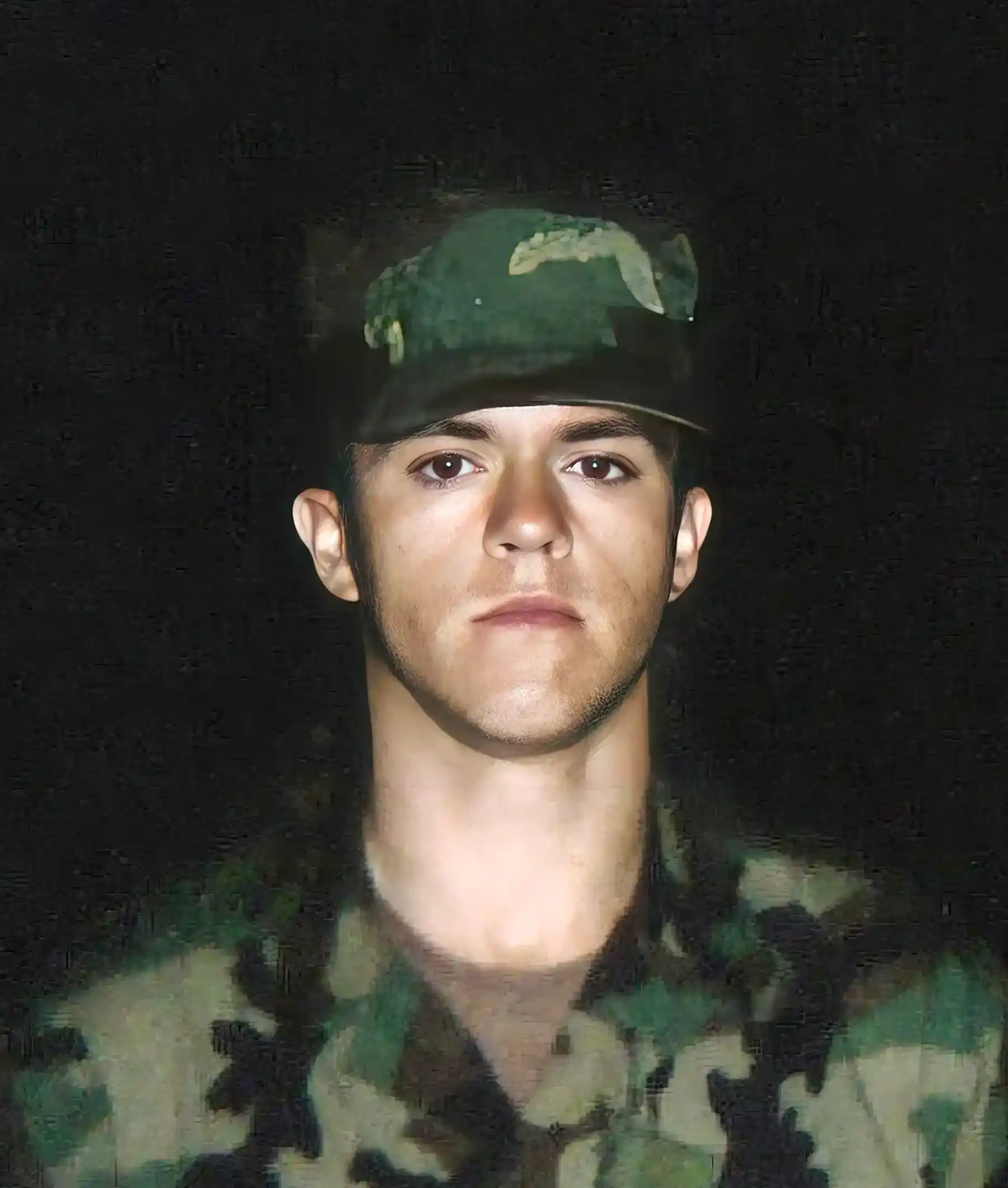A person wearing a camouflage military uniform and hat, posing for a portrait against a dark background.