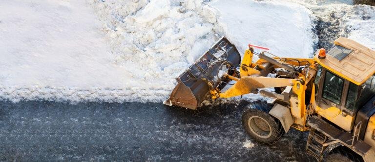 A yellow bulldozer efficiently clears snow from a road, expertly pushing it into a pile as part of comprehensive snow and ice removal for business parks.